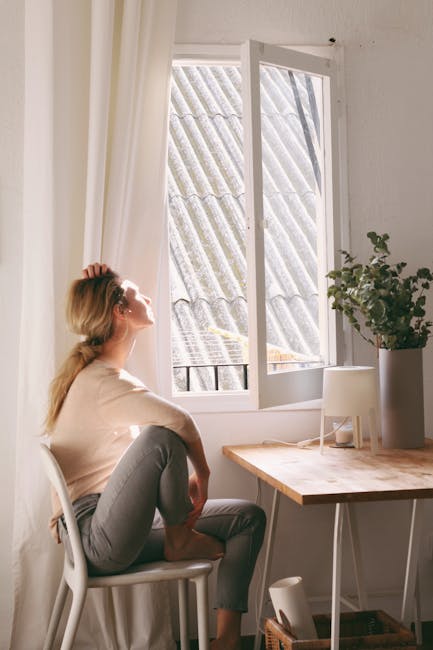 Person meditates at home, sitting in a calm position near the window.